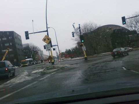 1985 Ford LTD Crown Victoria - A black sedan is seen from the rear on a wet street with traffic lights and signs visible.