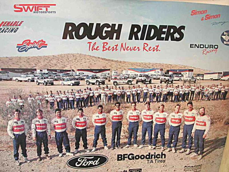 Group of people in racing uniforms standing in front of many trucks, vans, and trailers in a desert setting