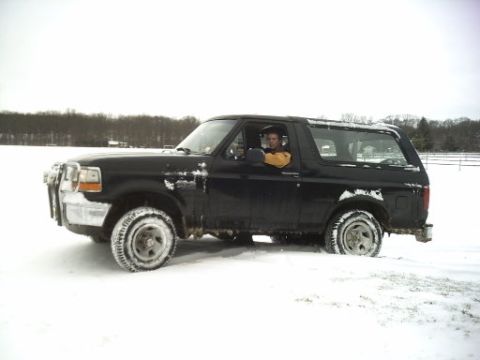 1996 Ford Bronco - Driver sits in a black 1996 Ford Bronco partially buried in snow.