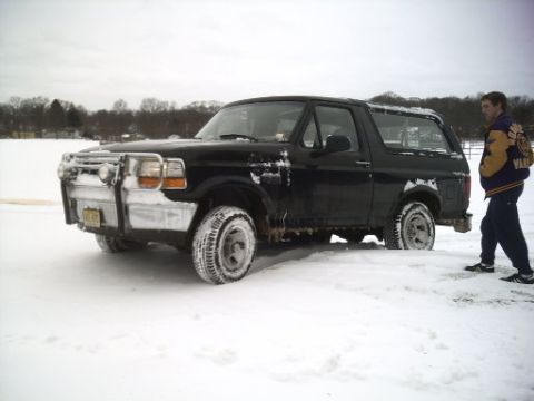 1996 Ford Bronco - A black 1996 Ford Bronco is partially stuck in the snow with a person standing nearby.