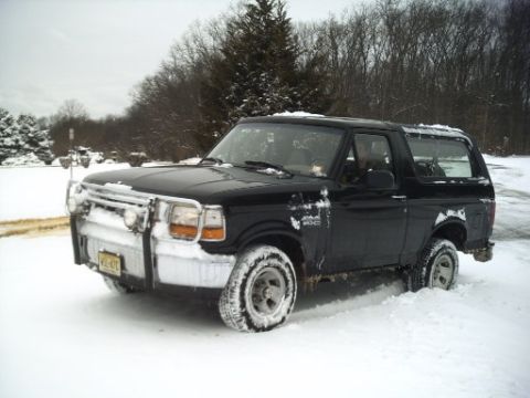 1996 Ford Bronco - A black 1996 Ford Bronco is partially buried in snow, showing its front quarter view with a brush guard.