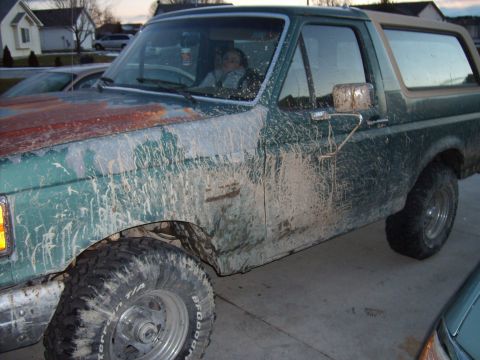 1989 Ford Bronco - This heavily mud-covered Ford Bronco is seen from the front quarter angle, with visible rust on its hood.