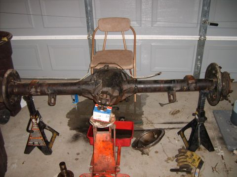 1989 Ford Bronco - A rear axle assembly is supported by jack stands in front of a garage door, with a chair positioned behind it.
