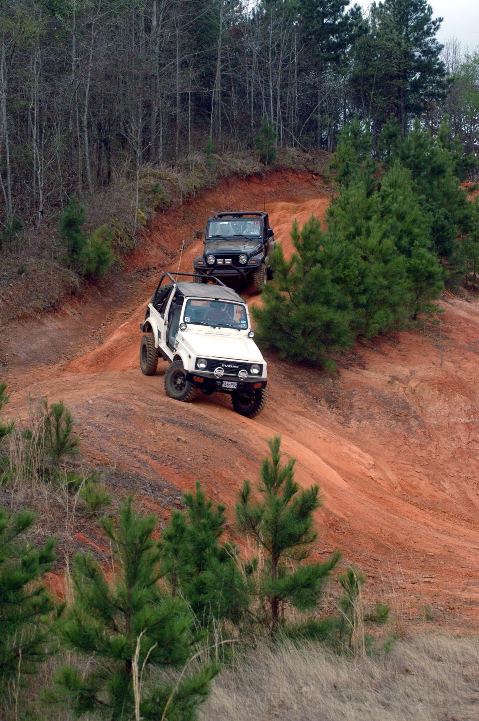 White 1987 Suzuki Samurai driving on a dirt hill with a black Jeep behind it
