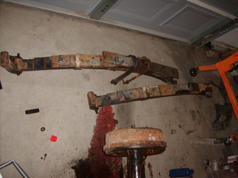 1989 Ford Bronco - Two heavily rusted leaf springs and a brake drum are visible on a concrete floor, possibly in a garage.