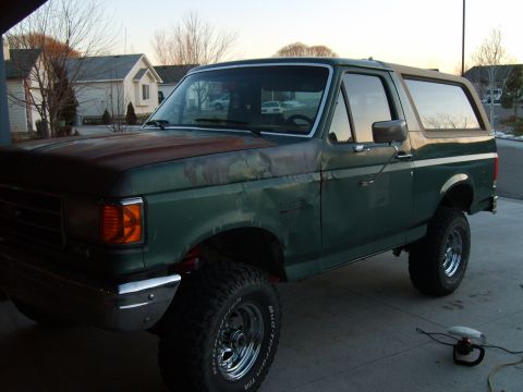 1989 Ford Bronco - This green Ford Bronco is parked in a driveway with houses in the background.