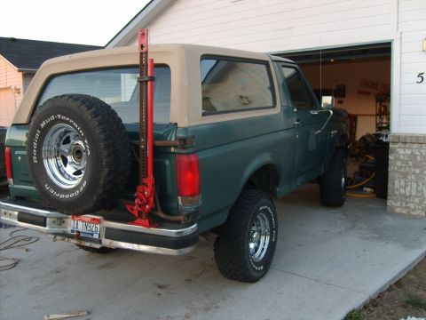 1989 Ford Bronco - Rear view of a green Ford Bronco with a tan removable top and a spare tire mounted on the tailgate.