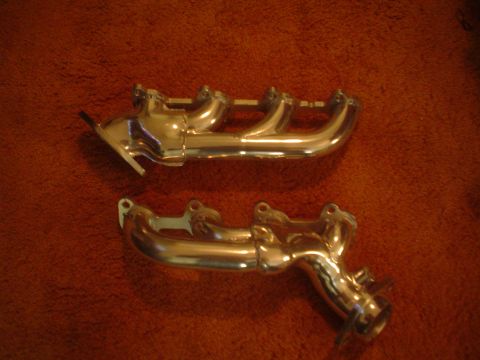 1996 Mercury Grand Marquis - Two shiny exhaust manifolds are displayed on a textured brown background. A website watermark is visible at the bottom right.