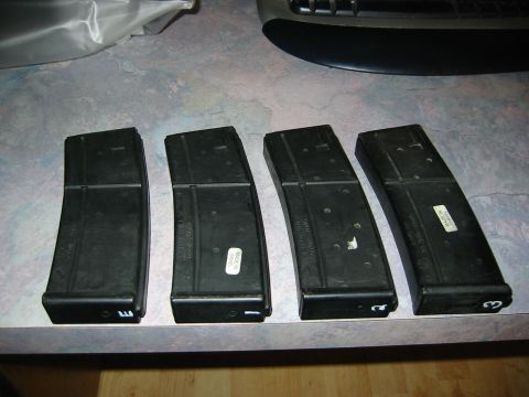 1996 Ford Bronco - Four black rifle magazines are laid out on a surface, with some showing white labels and markings.