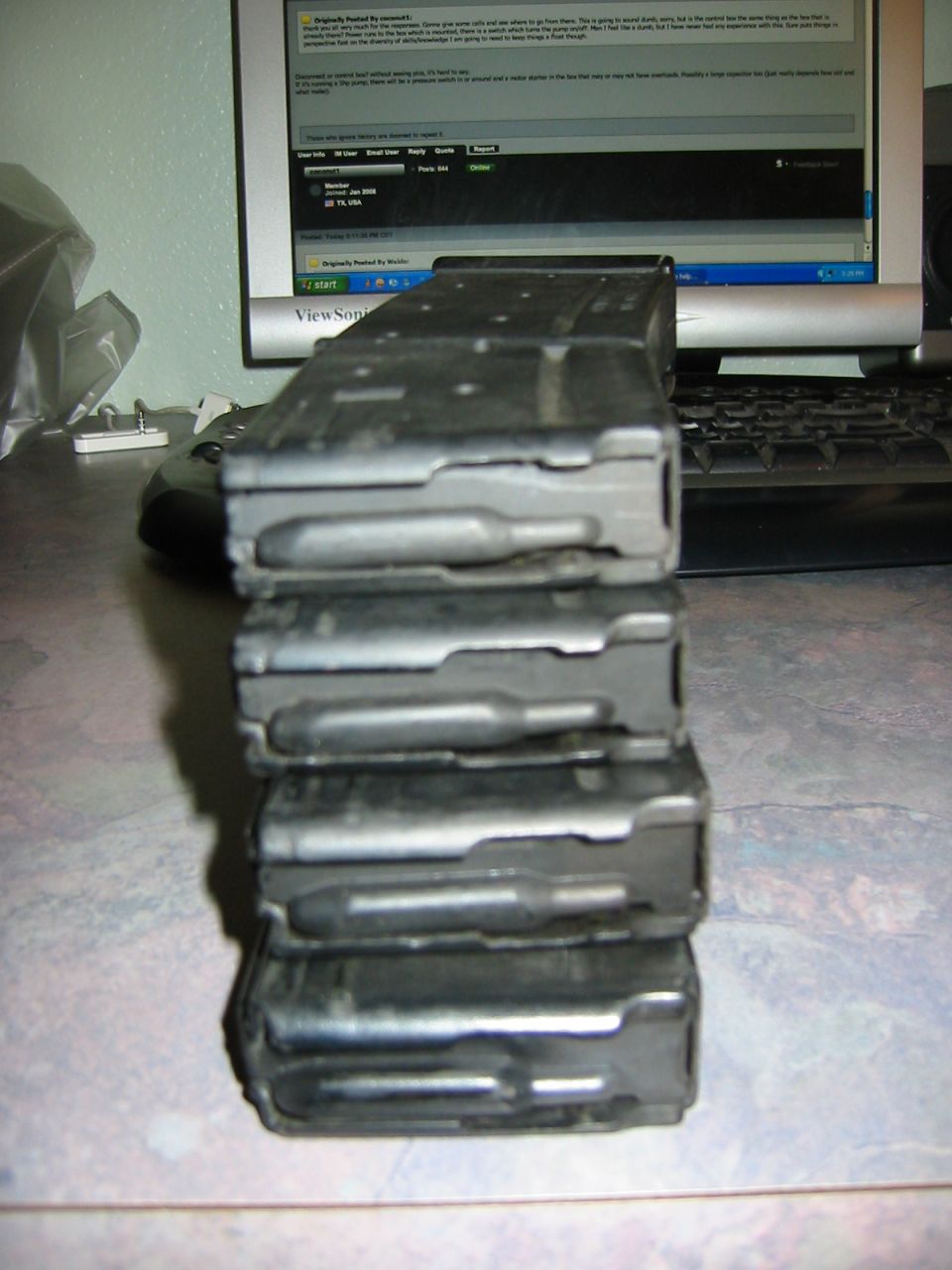 Stack of black rifle magazines on a desk in front of a computer monitor