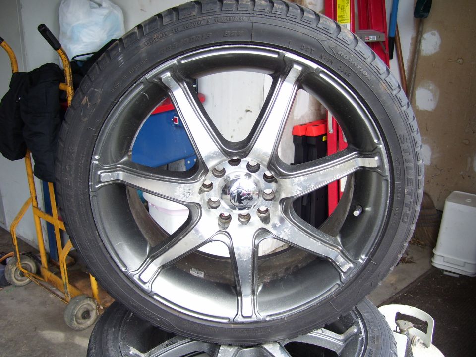 Chrome 7-spoke alloy wheel with low-profile tire standing in a garage