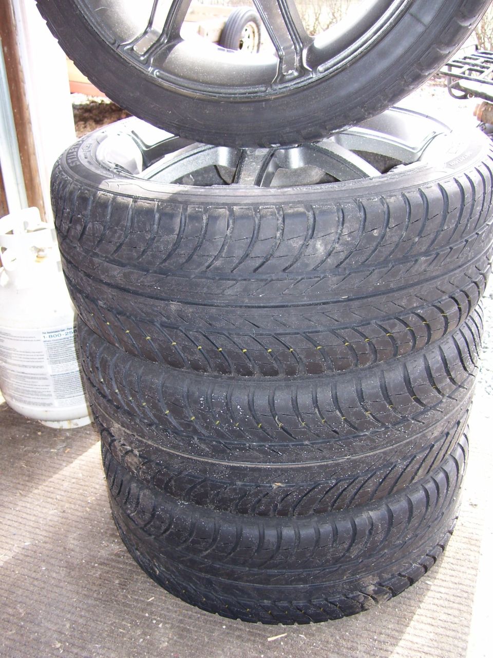 Stack of tires on alloy wheels beside a white propane tank
