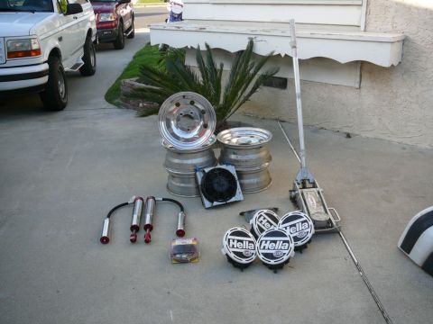 1988 Ford Bronco - A white 1988 Ford Bronco and a red pickup truck are parked on a driveway with various automotive parts laid out on the ground.