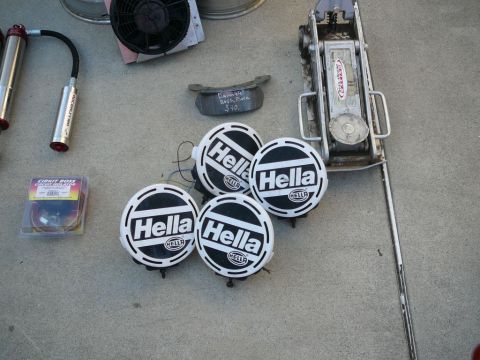 1988 Ford Bronco - A collection of automotive parts and tools, including Hella lights and a floor jack, are displayed on a concrete surface.