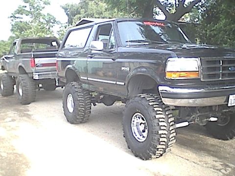 1987 Ford Bronco - A lifted black Ford Bronco from the early 1990s is shown alongside a lifted Ford pickup truck.