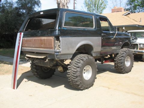 1987 Ford Bronco - Modified 1987 Ford Bronco with oversized tires, seen from the rear three-quarter angle.