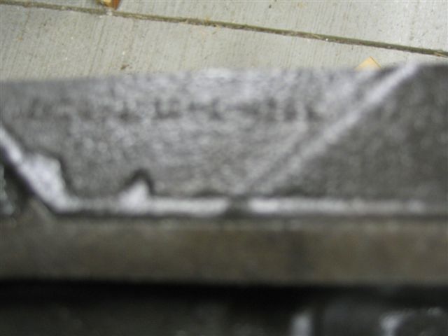 Close-up of a gray engine part with faint stamped numbers and lines