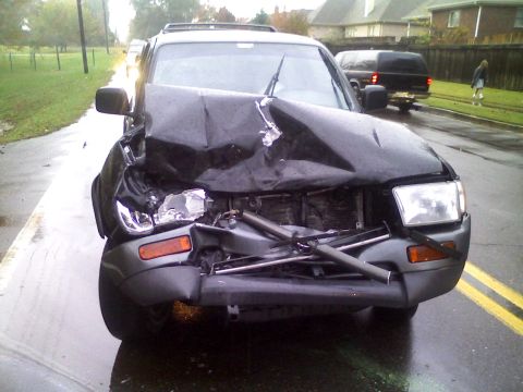 1996 Ford Bronco - A severely damaged black SUV sits on a wet road after an apparent collision, with another vehicle visible in the background.