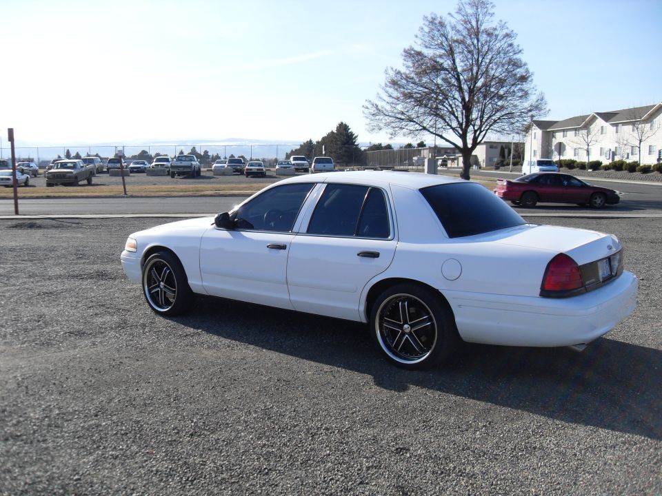 Rear three-quarter of a white Crown Victoria sedan with custom wheels