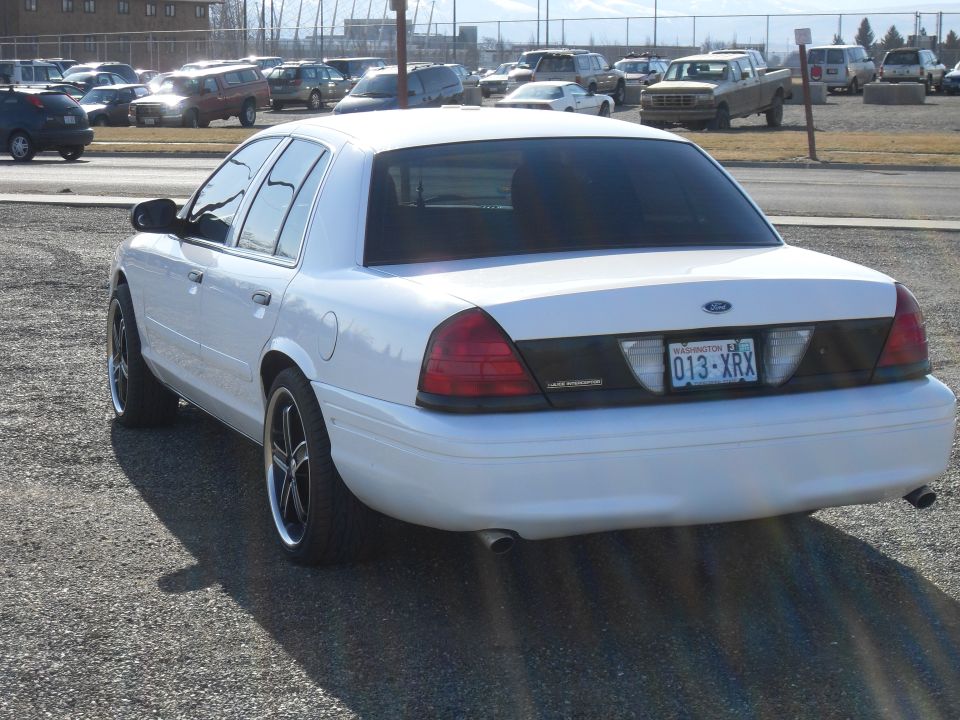 White Ford Crown Victoria rear 3/4 view with custom wheels and Washington plate, parked in lot