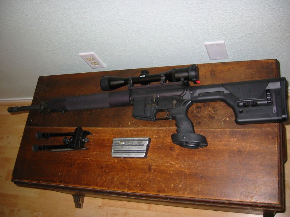Rifle with scope, bipod, and magazine on a wooden table