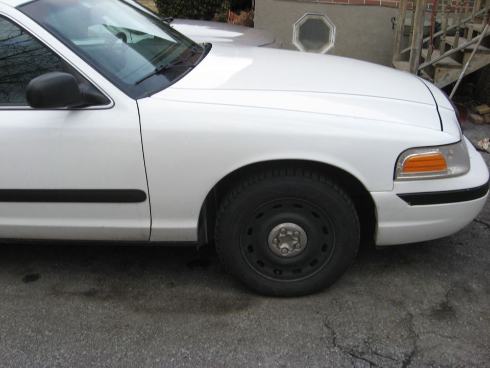 Front fender and black steel wheel of a white Ford Crown Victoria