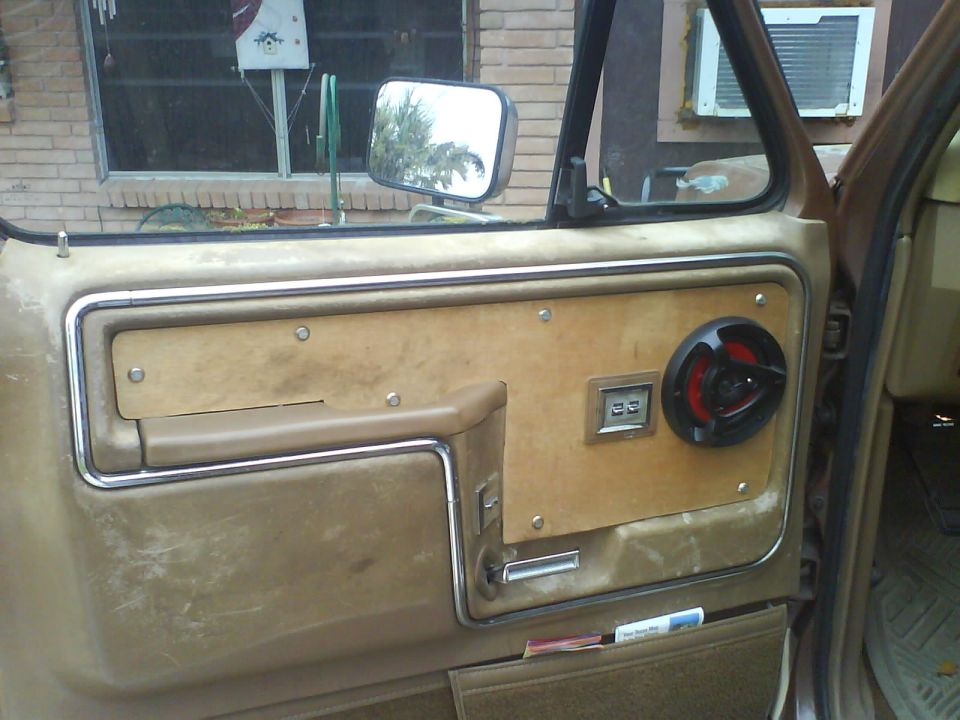 Tan door panel on open driver's door with wood insert, aftermarket speaker, and power window switches