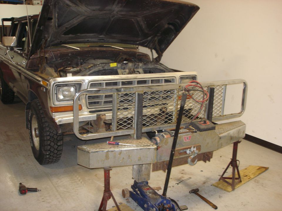 Brown 1979 Ford F-250 Crewcab with hood open, raised on jacks, a large aftermarket bumper and winch