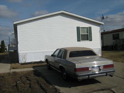 1988 Mercury Grand Marquis - A silver sedan is parked in front of a white mobile home on a cloudy day.
