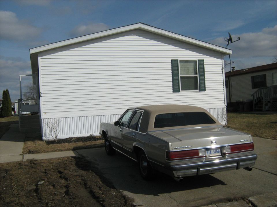 Silver sedan parked in driveway of a white mobile home. License plate reads BIK 5766