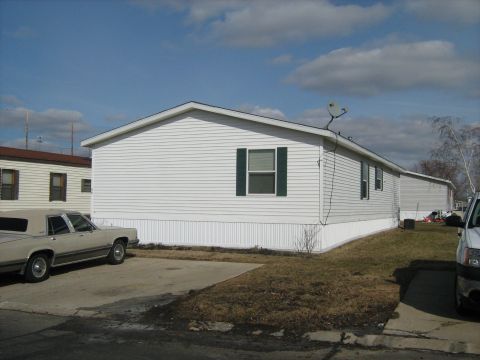 1988 Mercury Grand Marquis - white sided mobile home with green shutters sits on a lot with an older sedan and pickup parked nearby in winter.