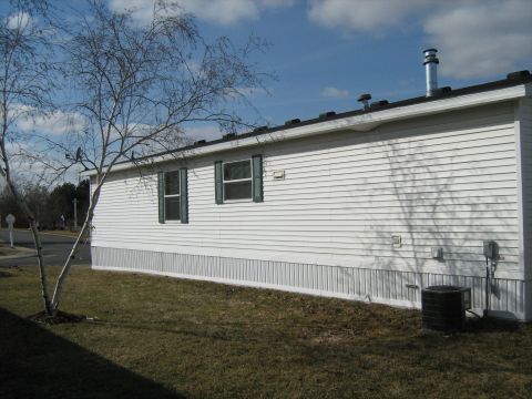 1988 Mercury Grand Marquis - A white mobile home is shown from the side, with a bare tree in the foreground and a blue sky with clouds above.
