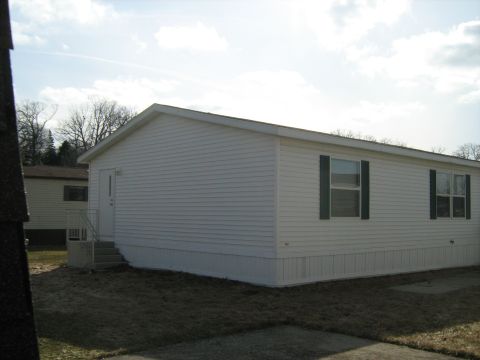 1988 Mercury Grand Marquis - A white mobile home with dark green shutters sits under a partly cloudy sky.