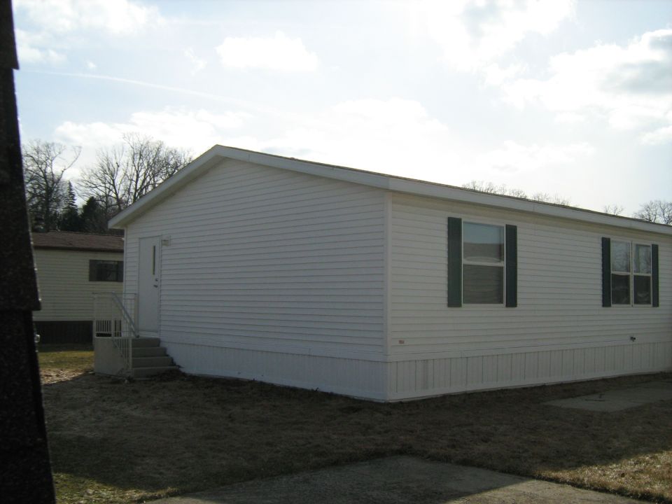 mobile home with white siding and green shutters, parked on a lot with dry grass