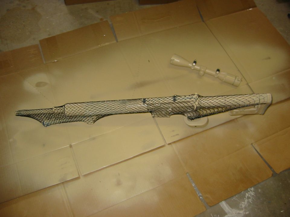 Rifle scope with netting and camouflage paint on cardboard