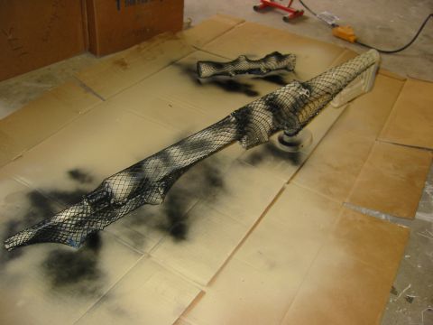 1996 Ford Bronco - Gun parts are being spray-painted with a camouflage pattern using netting as a stencil.