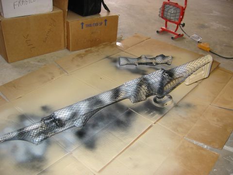 1996 Ford Bronco - A car part is being spray painted with a camouflage pattern using a mesh stencil.