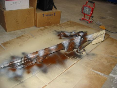1996 Ford Bronco - Parts of a rifle are laid out on cardboard, undergoing a camouflage paint job with a mesh stencil and spray paint.