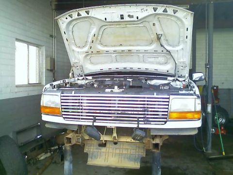 1996 Ford Bronco - The front grille and headlights of a white Ford F-Series truck are visible as it is raised on a service lift.