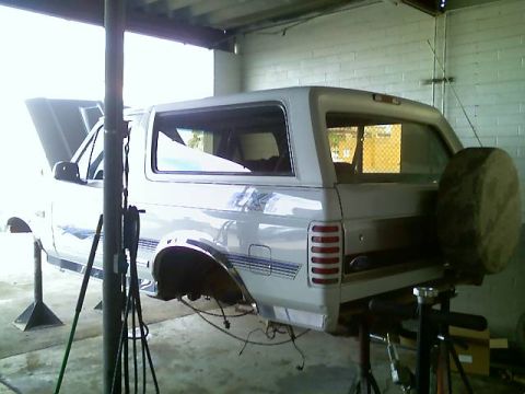 1996 Ford Bronco - This white Ford Bronco is elevated on jack stands with its hood open, revealing the engine bay.