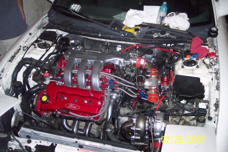 1994 Ford Probe - The engine bay of a white 1994 Ford Probe shows a modified engine with red valve covers and a turbocharger.