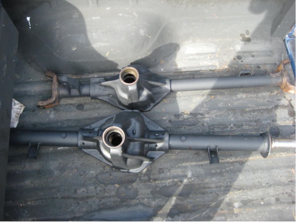 Two gray-painted solid axle housings lying in a truck bed, differential openings masked