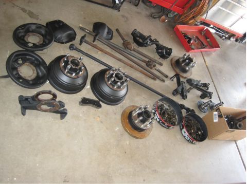 1996 Ford Bronco - Collection of vehicle axles, brake drums, and hubs, some SuperMotors branding, are displayed on a concrete surface.