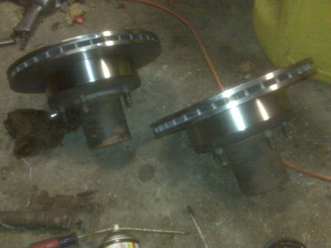 1995 Ford Bronco - Two brake rotors are shown on a concrete floor, possibly in a garage or workshop. One rotor is in the foreground on the left, and the other…