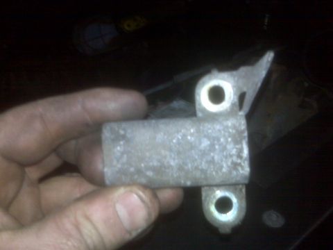1995 Ford Bronco - A hand holds a metal bracket with two circular holes and a rectangular body. The bracket appears to be part of a vehicle's assembly.