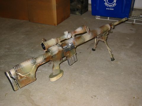 1996 Ford Bronco - A sniper rifle with a camouflage paint job is displayed on a concrete floor, with cardboard boxes and a blue recycling bin in the backgroun…
