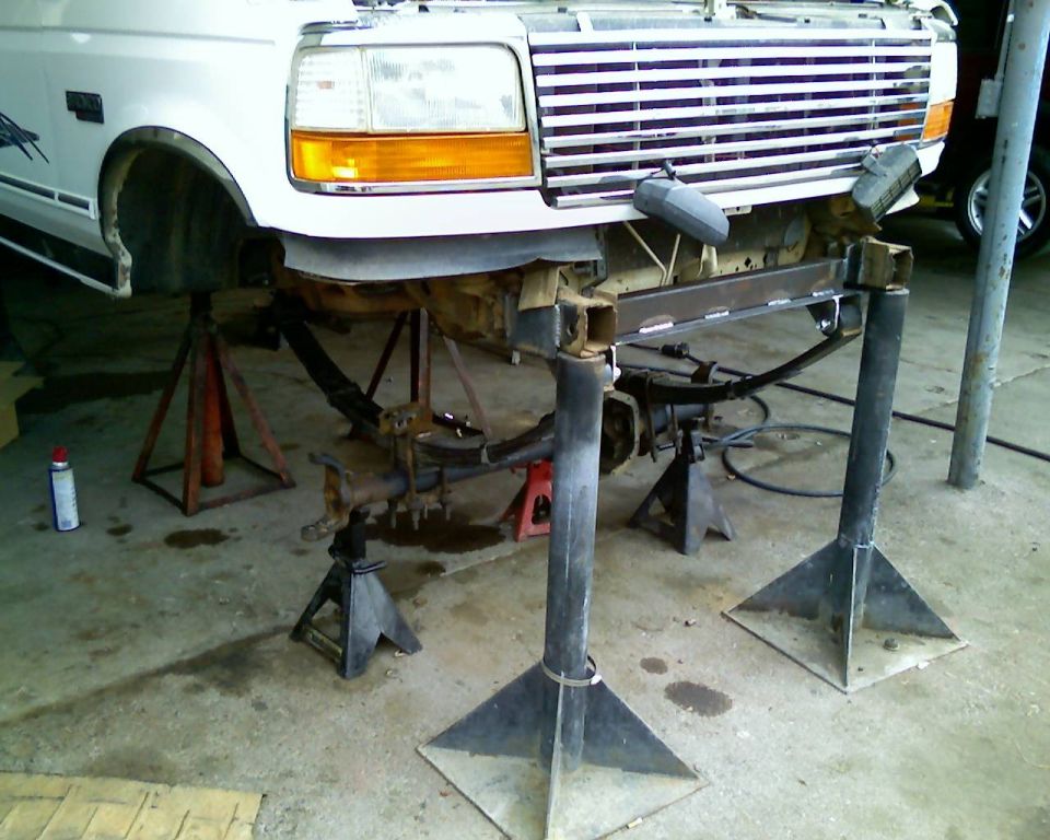 White Ford truck front raised on jack stands with front axle and leaf spring dropped out