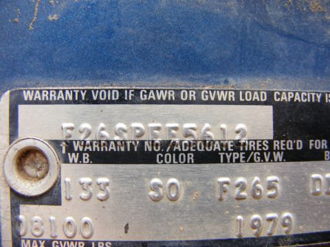 1985 Ford Bronco - A close-up view of a vehicle identification number (VIN) plate on a blue vehicle. The plate contains stamped text and numbers, including a…