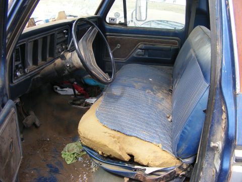 1985 Ford Bronco - Interior view of a blue Ford truck with a torn driver's seat and a dirty dashboard.
