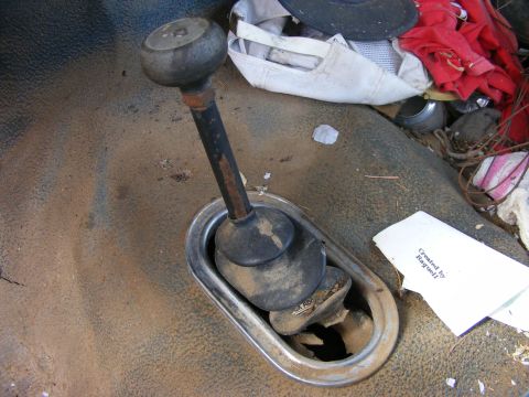 1985 Ford Bronco - A close-up view of a dirty, rusted gear shift lever and surrounding interior floor of what appears to be an older vehicle. A crumpled piece…